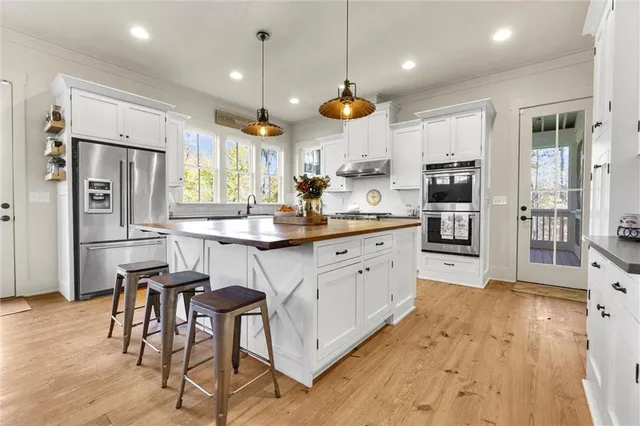 a kitchen with stainless steel appliances kitchen island granite countertop a stove a refrigerator a sink a dining table and chairs with wooden floor