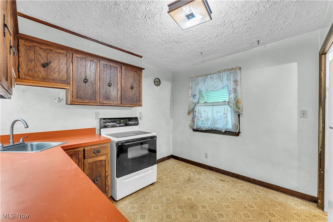 12931 Fruitside Road Garfield Heights, OH 44125 - Photo 5 of 15 Kitchen with white range with electric stovetop, a textured ceiling, light carpet, and sink