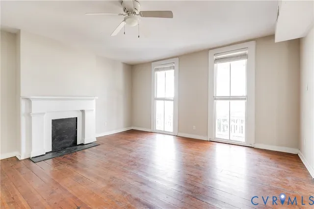 an empty room with wooden floor fireplace and windows