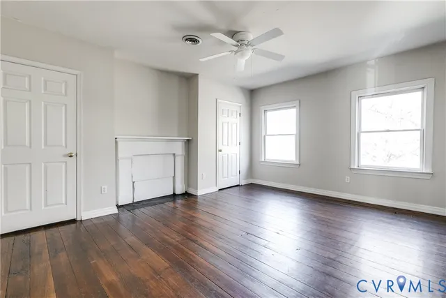 an empty room with wooden floor chandelier fan and windows