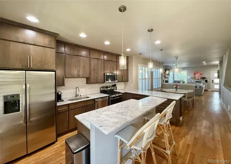 a kitchen with stainless steel appliances kitchen island granite countertop a kitchen island a stove a refrigerator a oven a sink with island a table and chairs