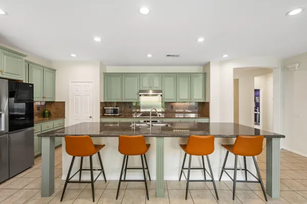 a kitchen with stainless steel appliances kitchen island granite countertop a dining table chairs refrigerator and sink
