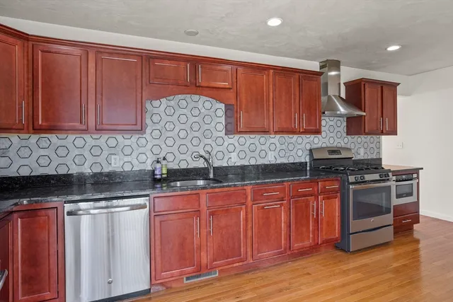 a kitchen with stainless steel appliances granite countertop a stove a sink dishwasher and a microwave oven with wooden cabinets