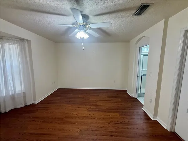 an empty room with wooden floor fan and windows