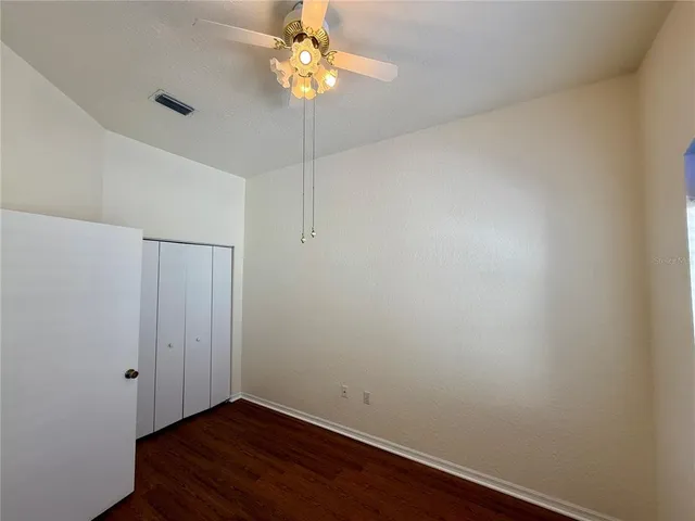 an empty room with a chandelier fan and wooden floor