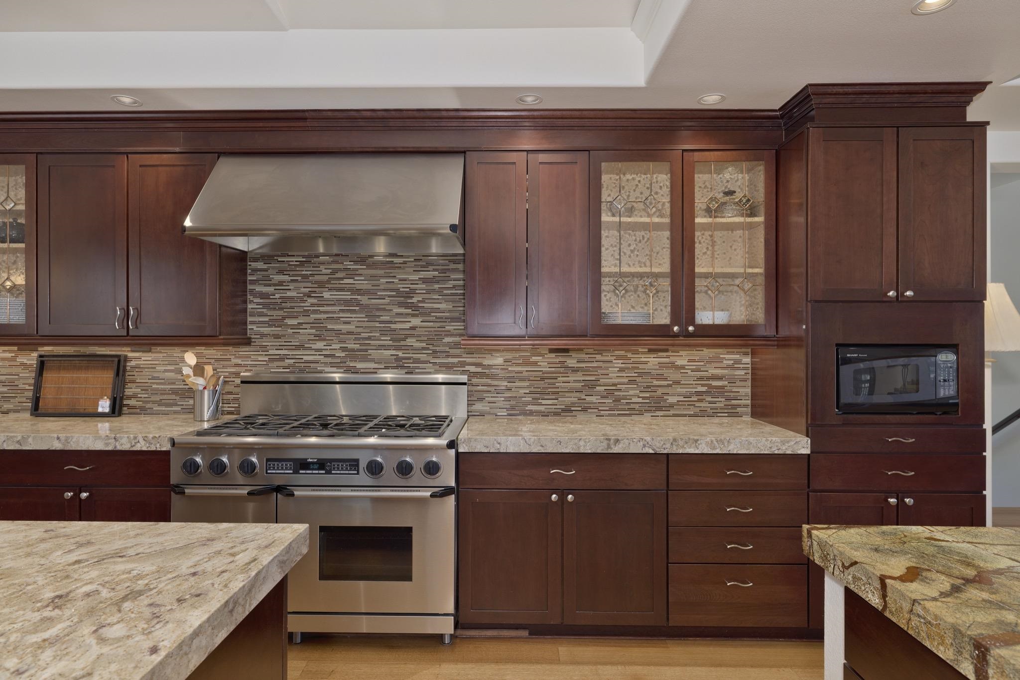 378 Ridge Way Mammoth Lakes, CA 93546 - Photo 13 of 43 Gourmet kitchen featuring a stainless steel range and coordinating hood, rich wood cabinetry with decorative glass inserts, mosaic tile backsplash, and light-toned countertops