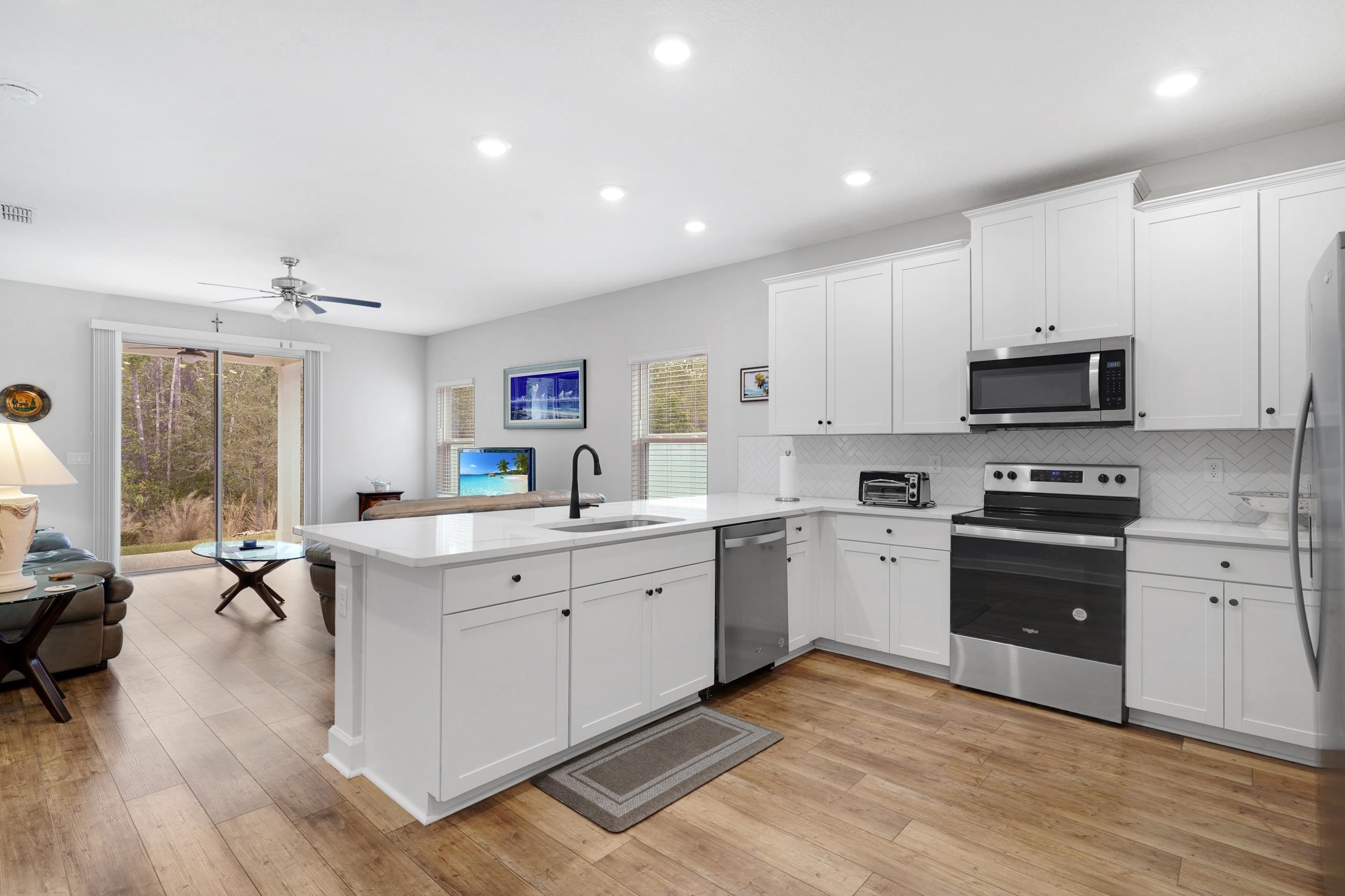 1014 Morgans Treasure Road St. Augustine, FL 32084 - Photo 31 of 31 a large white kitchen with a stove a sink dishwasher a microwave oven with white cabinets and wooden floor