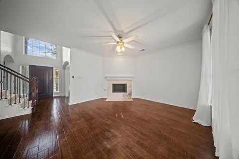 a view of an empty room with wooden floor and a ceiling fan