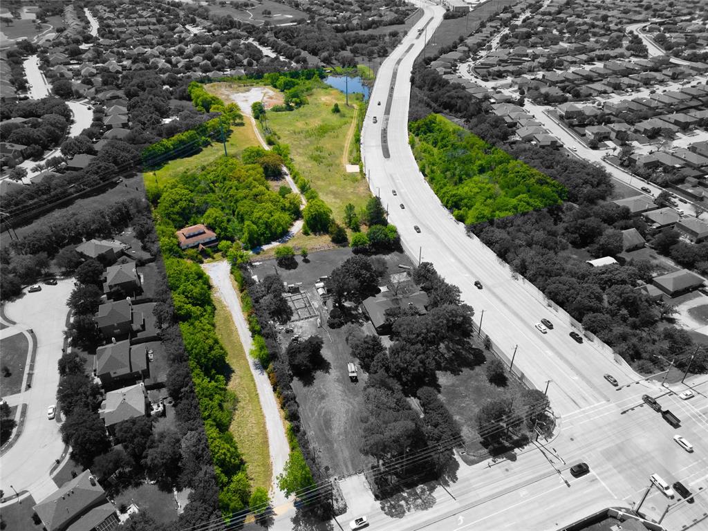 Aerial perspective showcasing a parcel of land featuring a pond, mature trees, and direct frontage to a multi-lane roadway