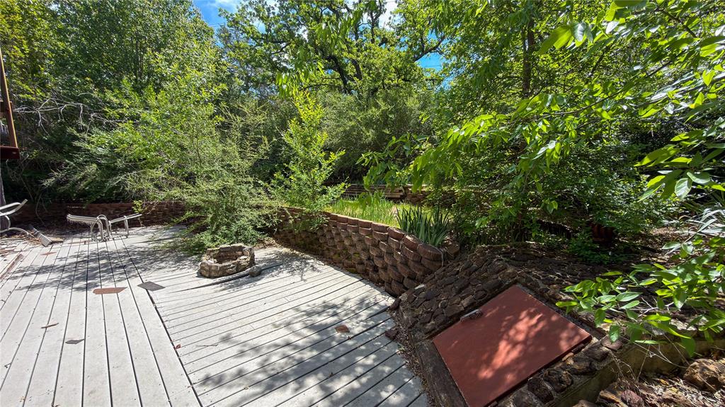 2900 Robinson Road Denton, TX 76210 - Photo 27 of 33 Outdoor decking with a built-in fire pit, surrounded by lush, mature landscaping and a retaining wall