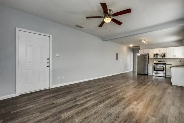 an empty room with wooden floor a ceiling fan and kitchen view