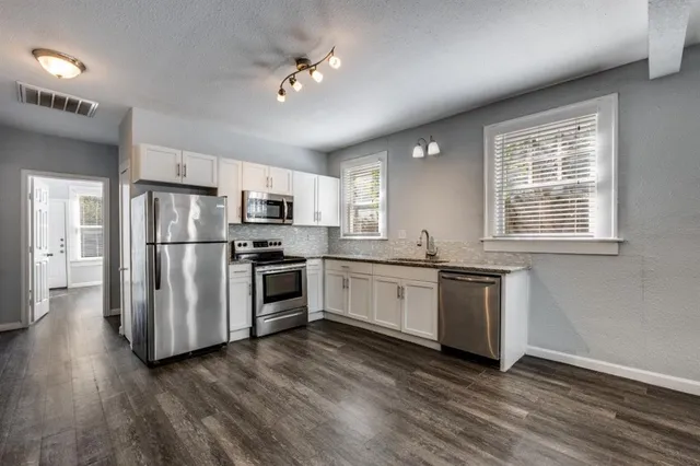 a kitchen with granite countertop stainless steel appliances a refrigerator cabinets and wooden floor