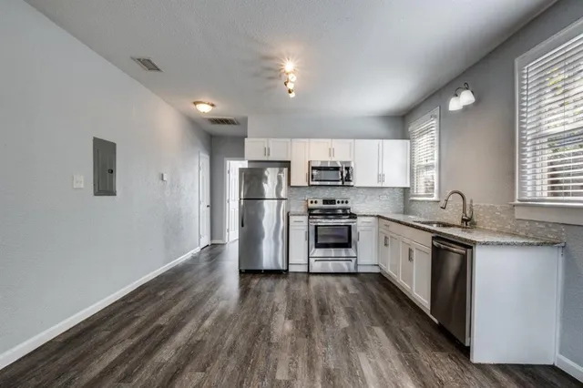 a kitchen with granite countertop a refrigerator oven a sink dishwasher and white cabinets with wooden floor