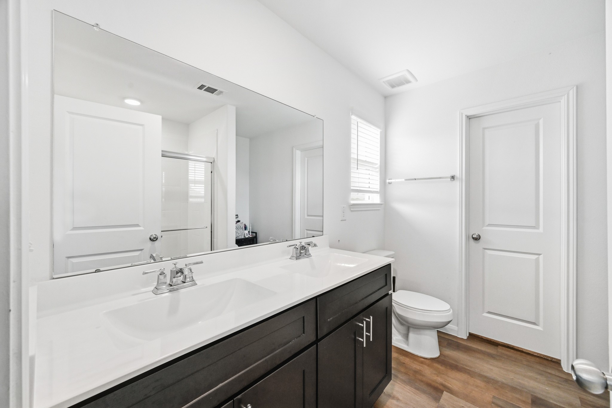 23427 Weir Box Road Hockley, TX 77447 - Photo 13 of 32 A spacious bathroom layout showcasing a large double-sink vanity with ample cabinet storage, an expansive mirror, and beautiful wood-look flooring.