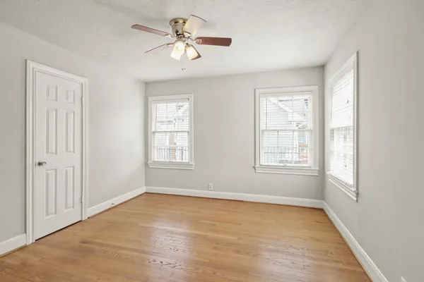 an empty room with wooden floor chandelier fan and windows