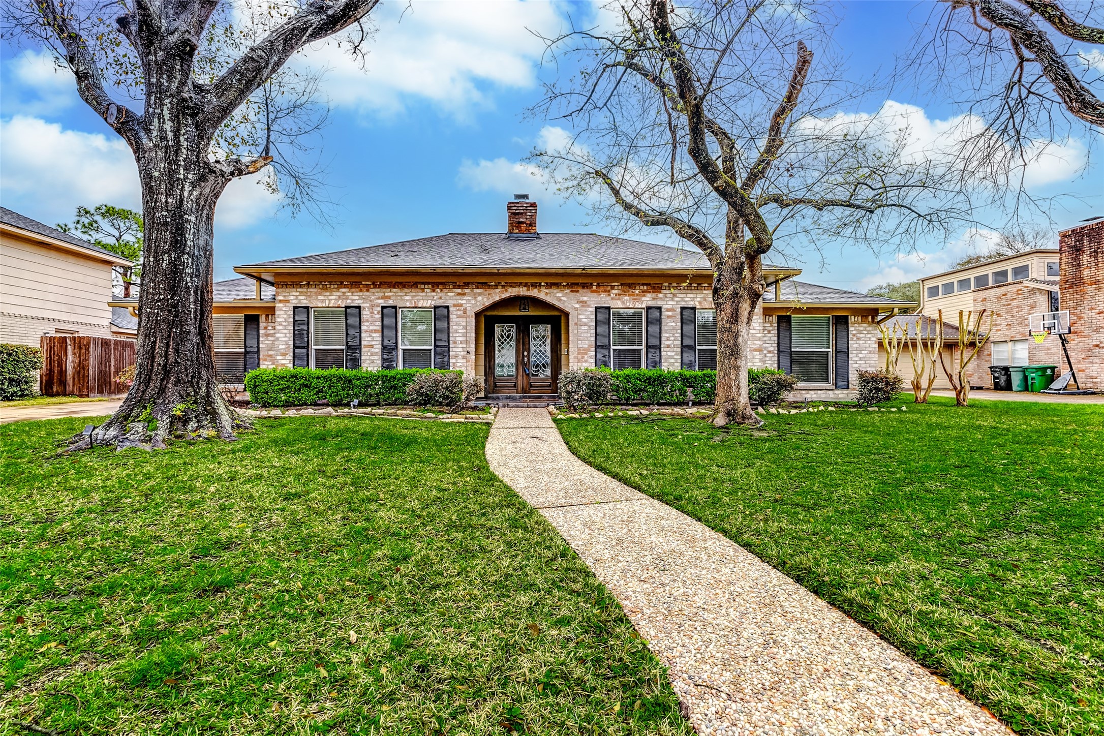 3022 Triway Lane Houston, TX 77043 - Photo 2 of 43 Nestled on a cul-de-sac, this home showcases a meticulously maintained lawn. A walkway cuts through the greenery, leading to the grand double front doors, set within a recessed alcove. A detached garage is set back on a long driveway.