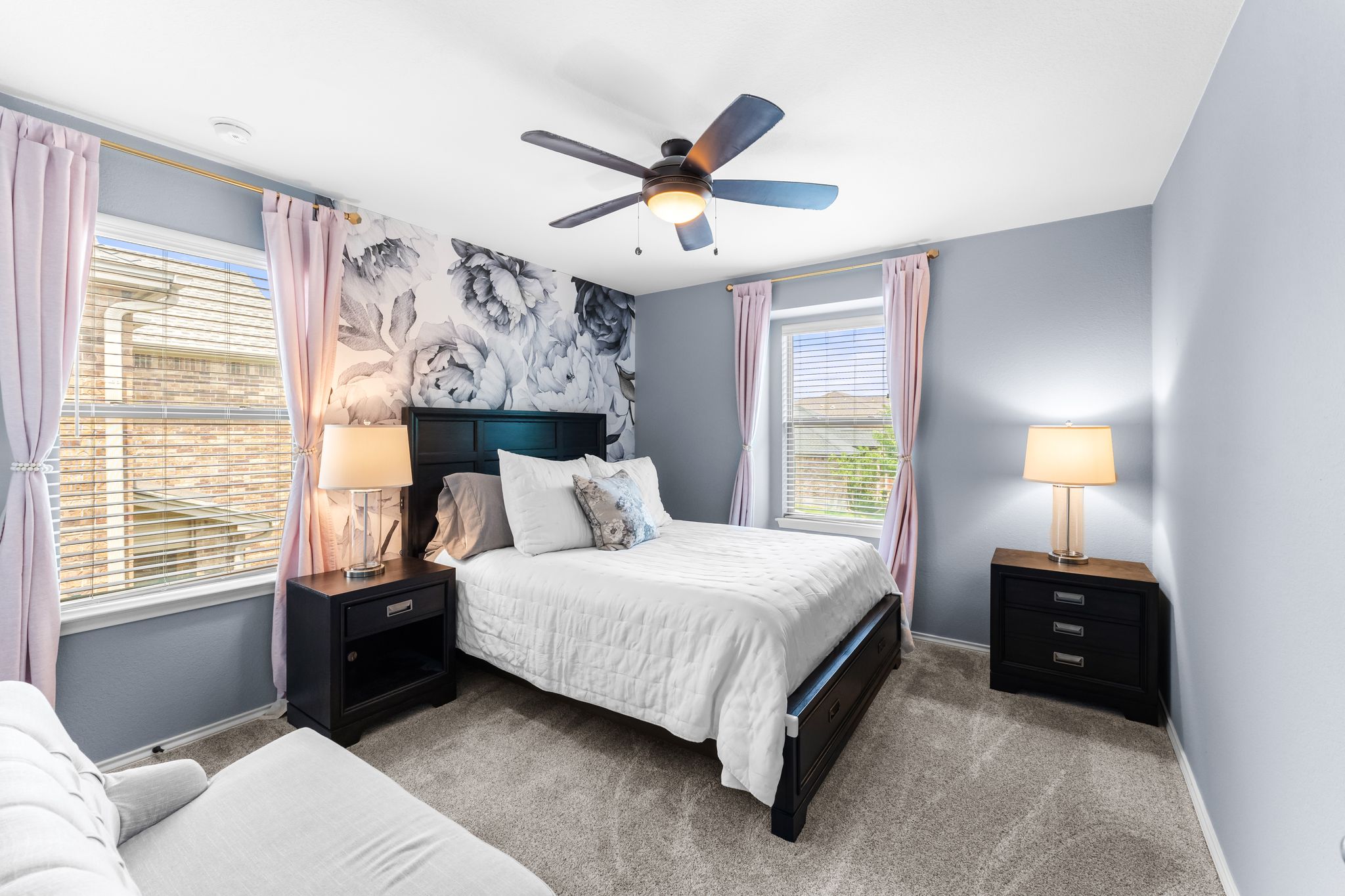 1133 Yellow Iris Road Leander, TX 78641 - Photo 28 of 37 Spacious bedroom featuring light grey carpeting, a prominent accent wall with floral detailing, and two large windows with blinds and light pink drapery