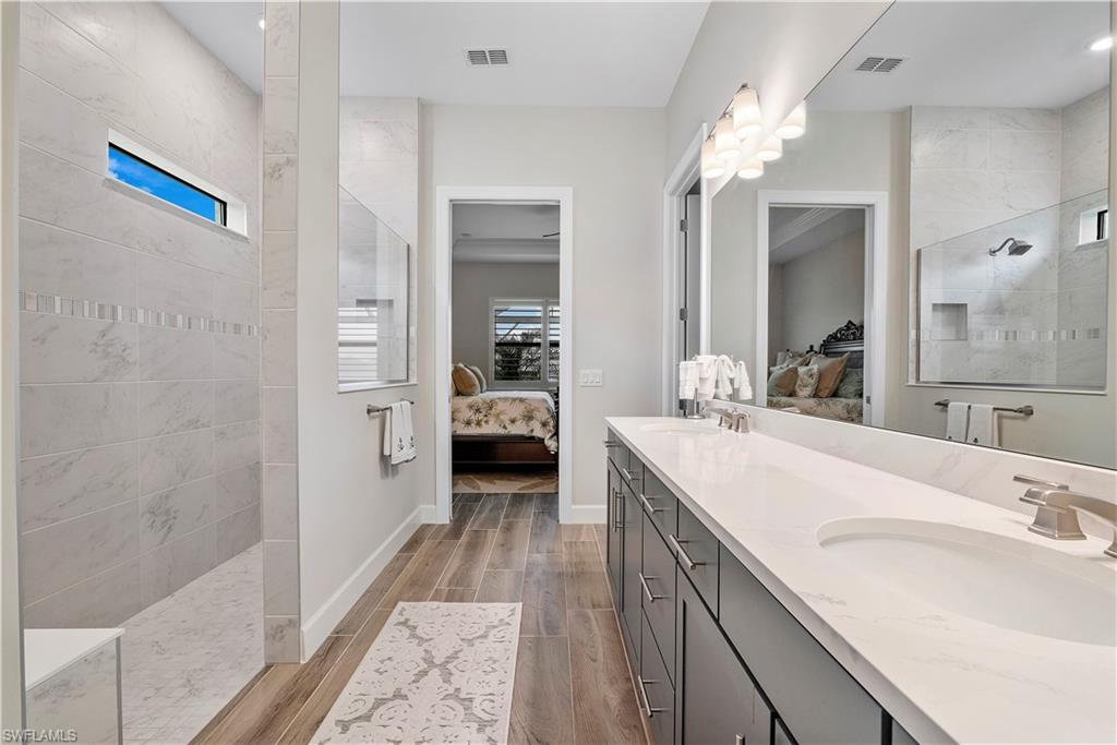 20150 Napa Loop Estero, FL 33928 - Photo 26 of 49 Bathroom with wood-type flooring, tiled shower, double sink, and vanity with extensive cabinet space