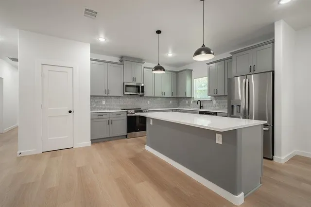 a kitchen with stainless steel appliances granite countertop a refrigerator a sink dishwasher a stove and white cabinets with wooden floor