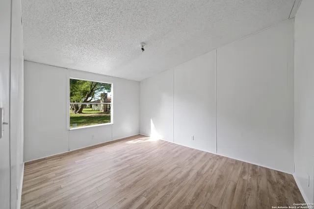 a view of an empty room with a window and wooden floor