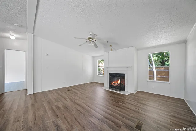 an empty room with wooden floor fireplace and windows