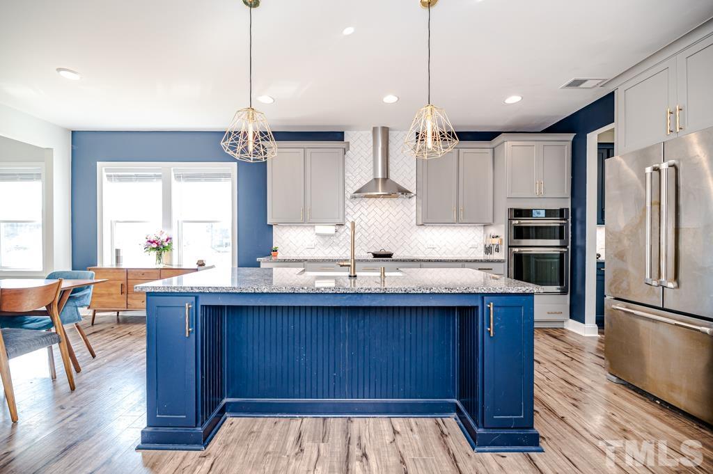 6712 Lucado Court Raleigh, NC 27603 - Photo 9 of 52 a kitchen with stainless steel appliances kitchen island granite countertop wooden floors sink and cabinets