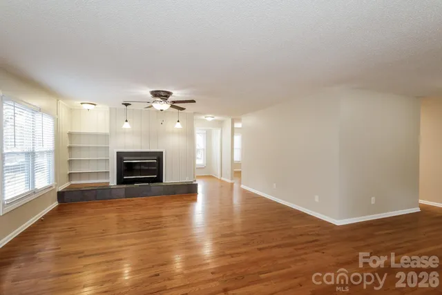 a view of an empty room with wooden floor fireplace and a window