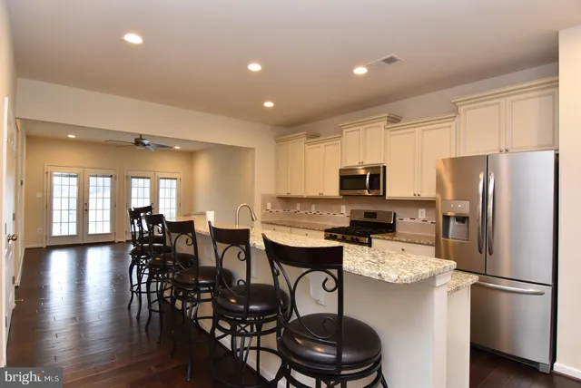 a kitchen with stainless steel appliances a refrigerator a stove a dining table and chairs with wooden floor