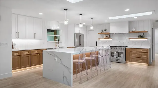 a large kitchen with stainless steel appliances kitchen island granite countertop a stove a sink a refrigerator and white cabinets with wooden floor