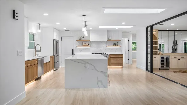 a kitchen with stainless steel appliances kitchen island granite countertop a refrigerator a sink a stove a dining table and chairs with wooden floor