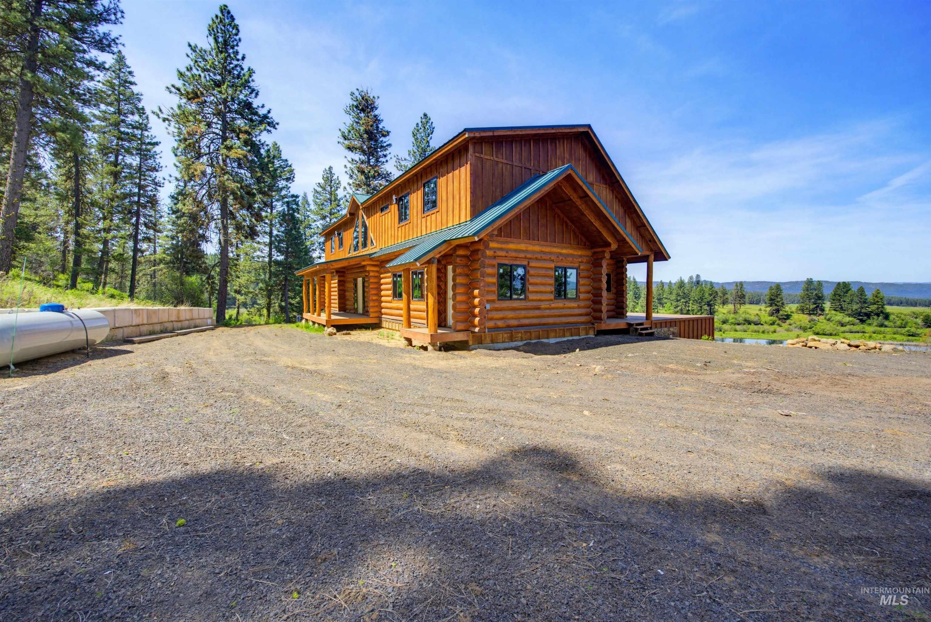 3322 Big Creek Road New Meadows, ID 83654 - Photo 11 of 50 Log home featuring a wood-sided exterior, green metal roof accents, multiple windows with black trim, an expansive gravel driveway, and a natural woodland setting