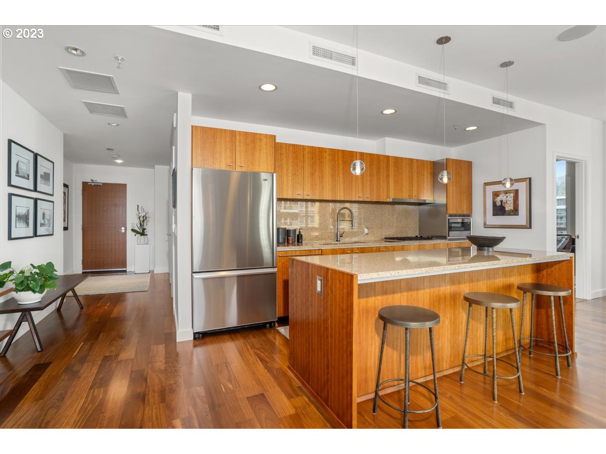 841 Southwest Gaines Street, Unit 1800 Portland, OR 97239 - Photo 21 of 39 a kitchen with stainless steel appliances granite countertop a refrigerator a sink dishwasher and a dining table with wooden floor