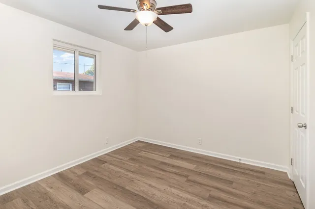 an empty room with wooden floor fan and windows