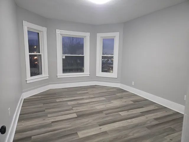 a view of an empty room with wooden floor and window