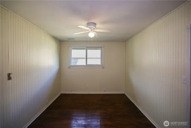 an empty room with wooden floor chandelier fan and windows
