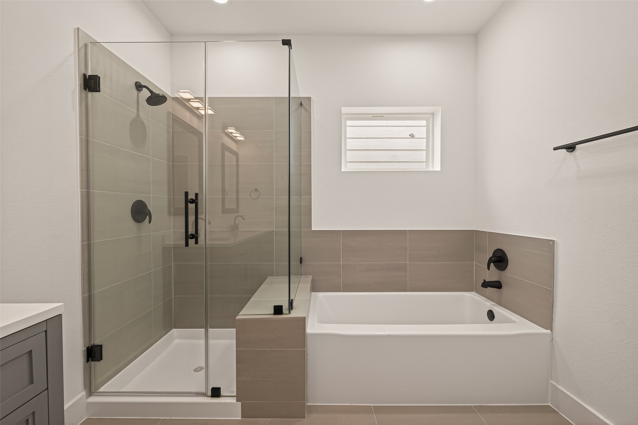 6808 Madrid Street Houston, TX 77021 - Photo 27 of 31 This modern bathroom features a sleek glass-enclosed shower and a separate bathtub, both with matte black fixtures. The neutral tiles and bright lighting create a clean, contemporary look.