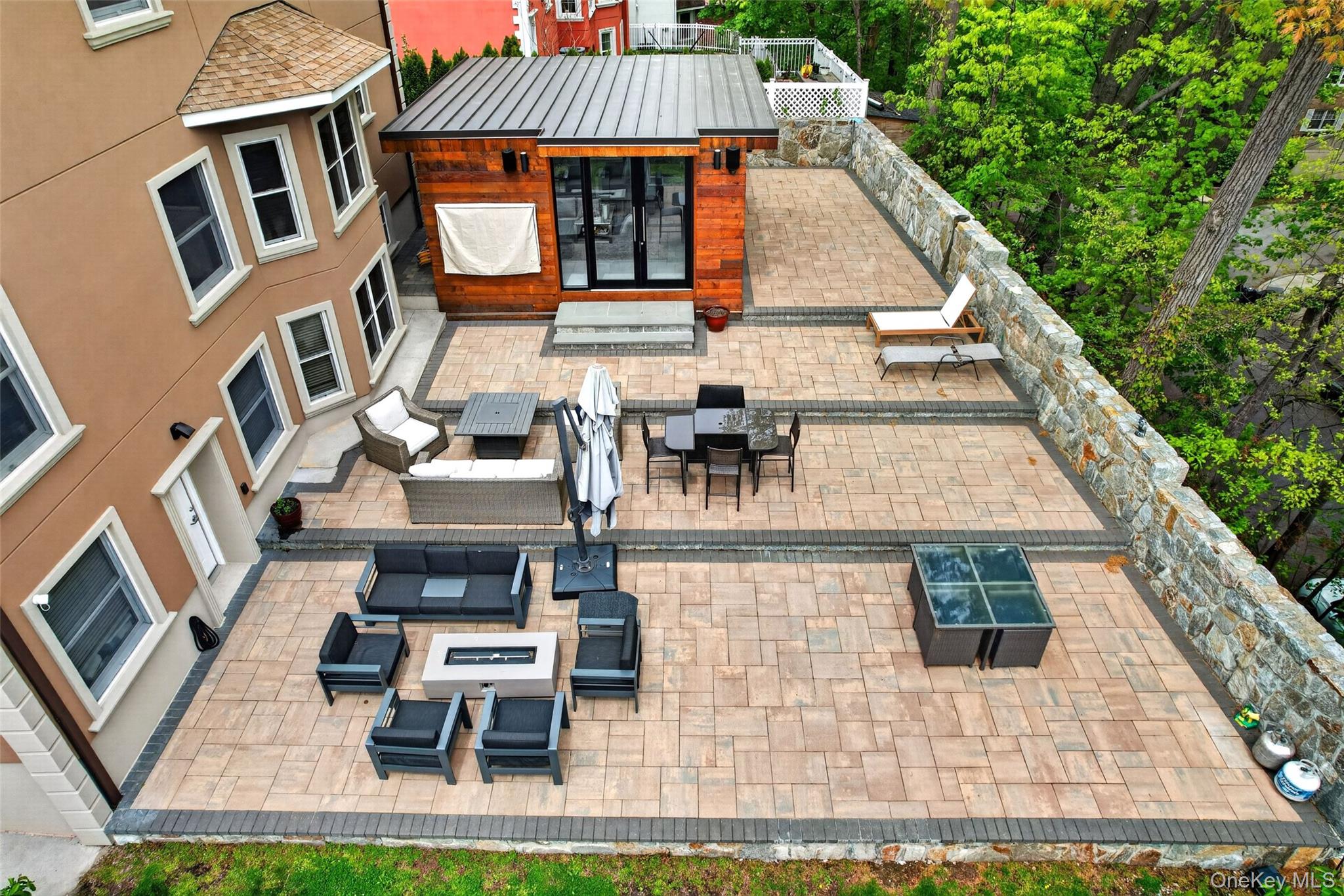 65 Wildway Bronxville, NY 10708 - Photo 16 of 42 Multi-level paver patio featuring stone retaining walls and a detached structure with wood siding and a metal roof
