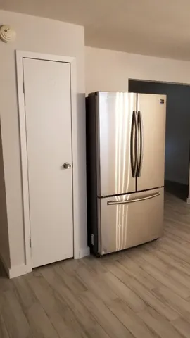 a view of a refrigerator in kitchen and an empty room with wooden floor