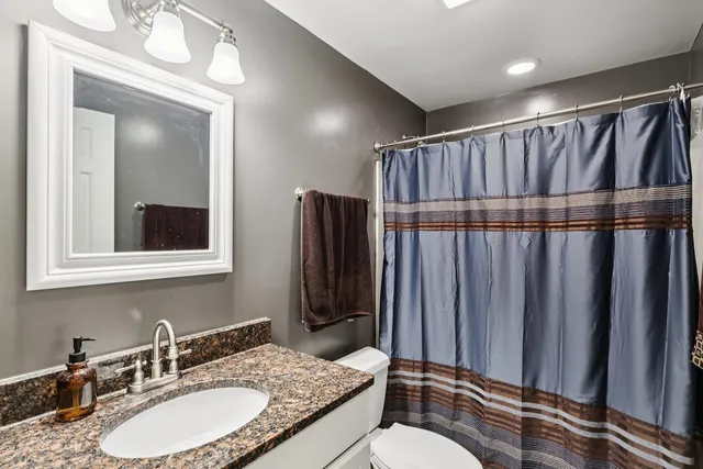 a bathroom with a granite countertop sink toilet a mirror a vanity and shower