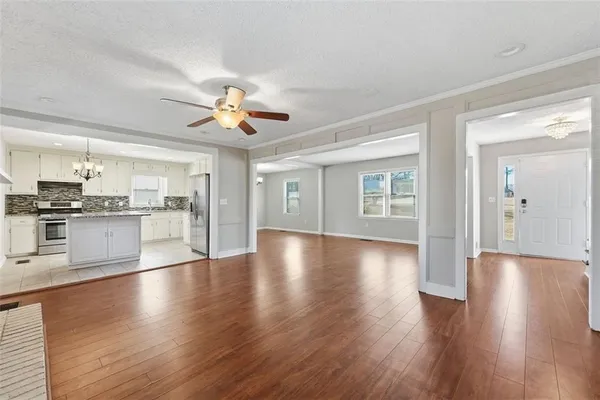 a view of an empty room with kitchen view and wooden floor