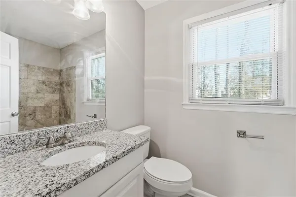 a bathroom with a granite countertop sink toilet a large mirror and a window