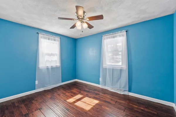 an empty room with wooden floor fan and windows