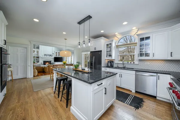 a open kitchen with stainless steel appliances granite countertop a stove top oven a refrigerator a sink and a fireplace with wooden floor