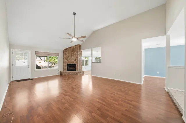 an empty room with wooden floor fireplace and windows