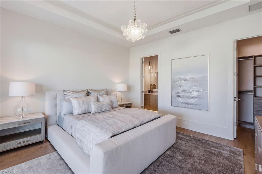 529 Neapolitan Way Naples, FL 34103 - Photo 21 of 26 a spacious bedroom with a bed and a chandelier