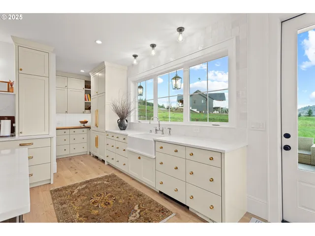 a large white kitchen with granite countertop a stove a sink and white cabinets with wooden floor