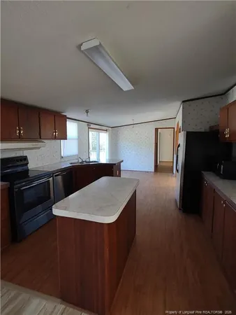 a kitchen with stainless steel appliances granite countertop a sink a stove a refrigerator a microwave oven and a dining table with wooden floor