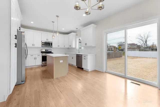 a kitchen with stainless steel appliances granite countertop a refrigerator a sink a stove and white cabinets with wooden floor