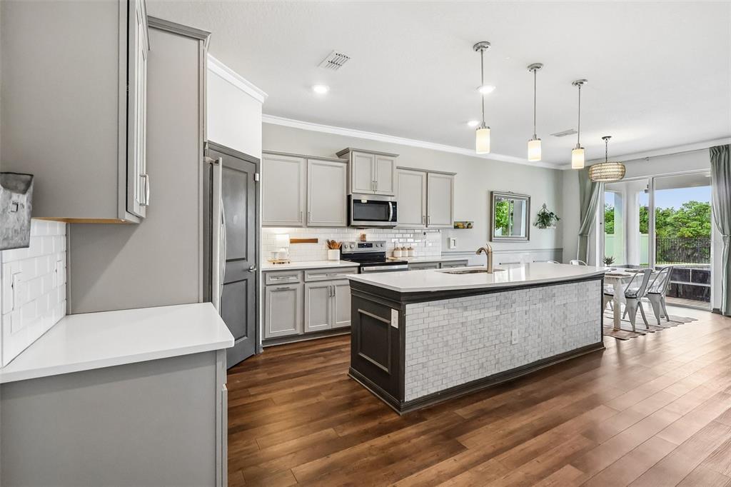2575 Auburn Ridge Drive Apopka, FL 32712 - Photo 8 of 48 a large kitchen with stainless steel appliances kitchen island granite countertop a stove a sink a refrigerator a microwave oven and a dining table with wooden floor