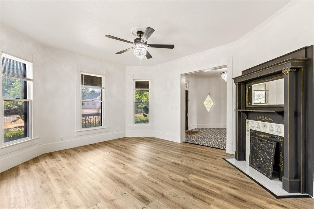 1005 North Trinity Street Decatur, TX 76234 - Photo 7 of 39 Bay window configuration, wood-finish flooring, decorative fireplace with tiled hearth, ceiling fan with crystal light fixture, and wide entryways